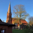 Die Kirche in Estorf, ein roter Backsteinbau mit hohem Turm, umgeben von Bäumen im Sonnenlicht.