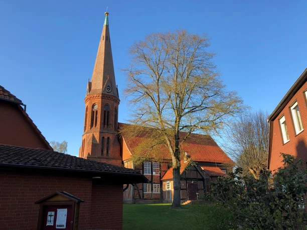 Die Kirche in Estorf, ein roter Backsteinbau mit hohem Turm, umgeben von Bäumen im Sonnenlicht.