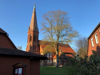 Kirche Estorf Die Kirche in Estorf, ein roter Backsteinbau mit hohem Turm, umgeben von Bäumen im Sonnenlicht.