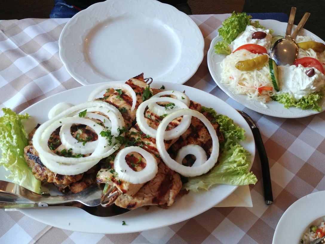 Griechische Fleischplatte mit gegrilltem Fleisch, frischen Zwiebelringen und Beilagensalat.