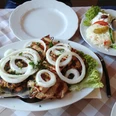 Griechische Fleischplatte mit gegrilltem Fleisch, frischen Zwiebelringen und Beilagensalat.
