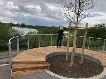 Aussichtsplattform Leeser Seenplatte Ein gebogener, hölzerner Steg mit Geländer führt zu einem Aussichtspunkt mit Blick auf einen See.