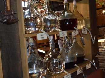 Liebharts Fachwerkdorf-Sudhaus 2 Verschiedene Glasballons mit Zapfhähnen, gefüllt mit Obstbränden, sind in stilvoller Holzwand eingelassen.