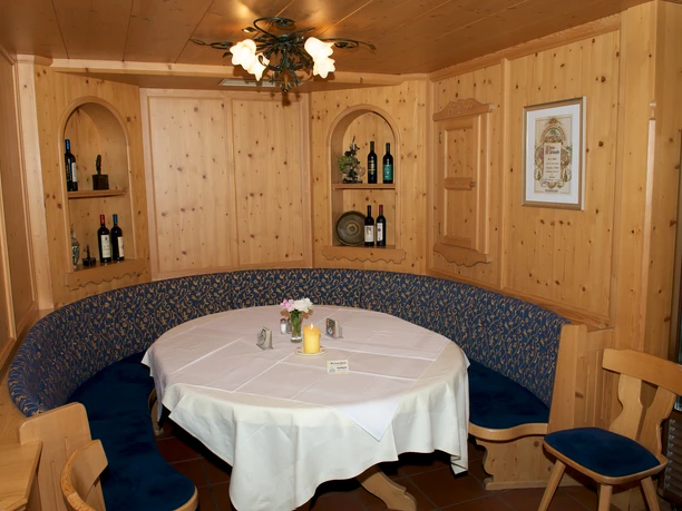 Da Nico in Farchant - Sitzecke Runder Tisch mit weißem Tischtuch, darum eine runde Eckbank vor gemütlicher Holzwand