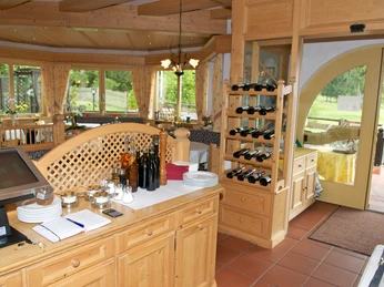 Da Nico in Farchant - Innenbereich Ein Holztresen mit der Kasse, Notizbuch und Ölflaschen im Vordergrund, etwas weiter hinten ein Holzregal mit Weinflaschen