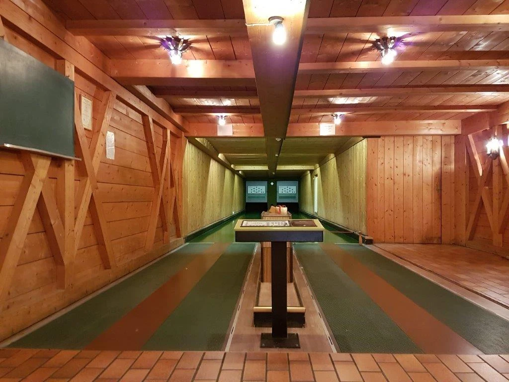 Farchanter Kegelkeller Zwei Kegelbahnen nebeneinander im Kegelkeller Farchant . Vorne steht ein Tisch, links an der Wand ist eine Tafel befestigt und an der Decke befinden sich Lampen