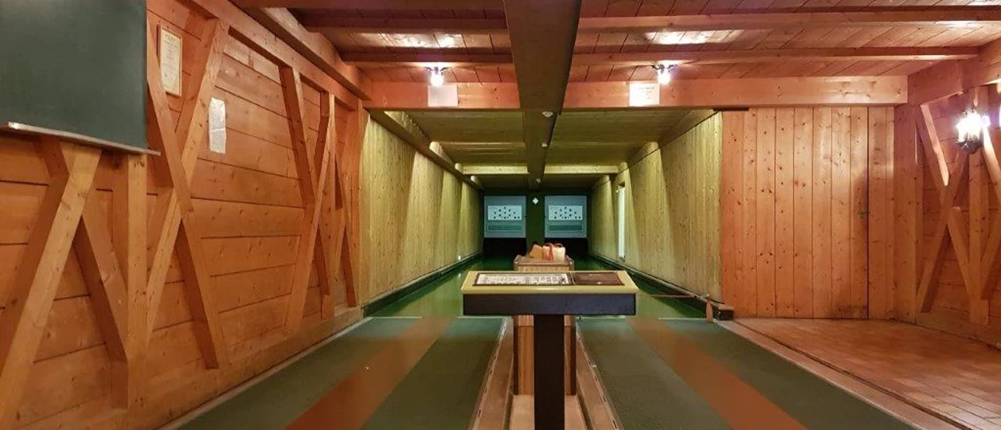 Farchanter Kegelkeller Zwei Kegelbahnen nebeneinander im Kegelkeller Farchant . Vorne steht ein Tisch, links an der Wand ist eine Tafel befestigt und an der Decke befinden sich Lampen