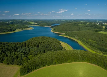 Große Dhünn- Talsperre <p>Luftaufnahme einer bewaldeten Halbinsel, umgeben von einem blau schimmernden See unter klarem Himmel.</p>