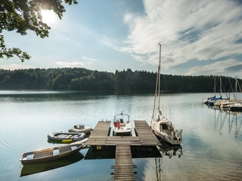 Bevertalsperre Anlegestelle mit Booten an einem ruhigen See, umgeben von bewaldeten Hügeln unter blauem Himmel.