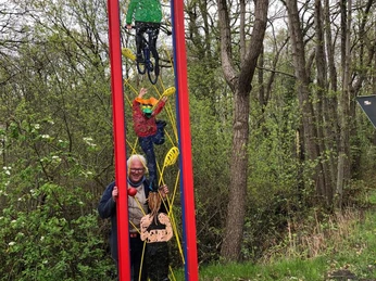 Lieblingsort Unterster Weg - Aktivrahmen Ein roter Metallrahmen mit angebrachten Personenfiguren steht im Wald; eine Frau posiert daneben.