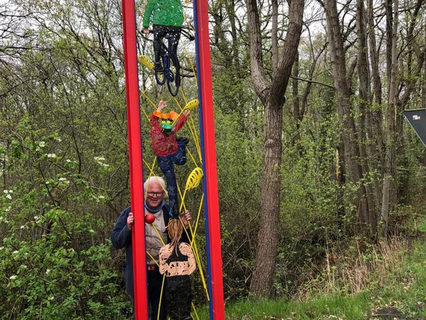 Lieblingsort Unterster Weg - Aktivrahmen Ein roter Metallrahmen mit angebrachten Personenfiguren steht im Wald; eine Frau posiert daneben.