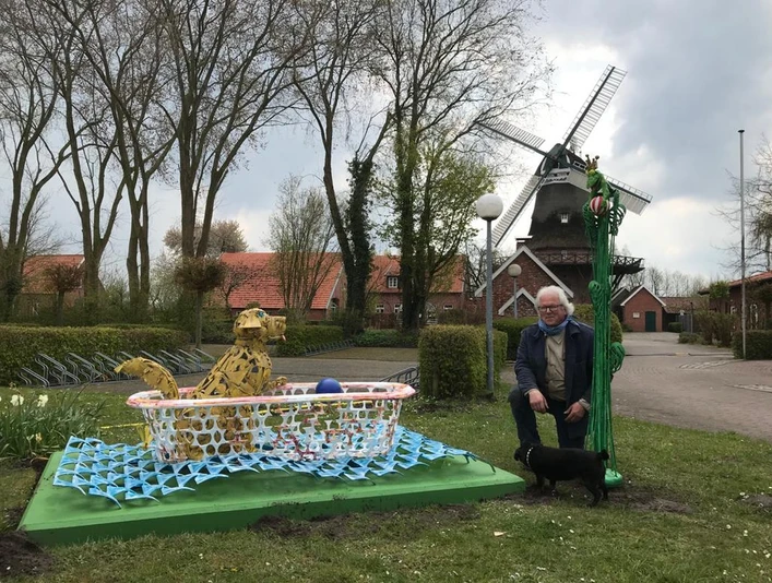 Lieblingsort Freibad Hengstforde Ein Mann kniet neben einem Hund vor einem dekorativen, mosaikartigen Aufsteller, im Hintergrund eine Windmühle.
