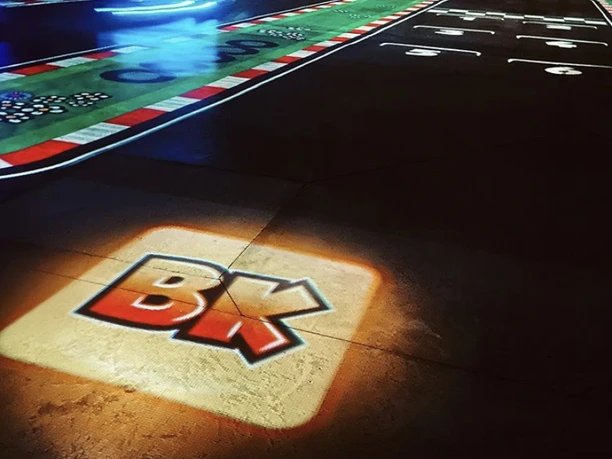 Das Bild zeigt eine detailreiche Modellrennstrecke mit farbigen Markierungen und dem leuchtenden Logo "BK" auf dem Boden.
