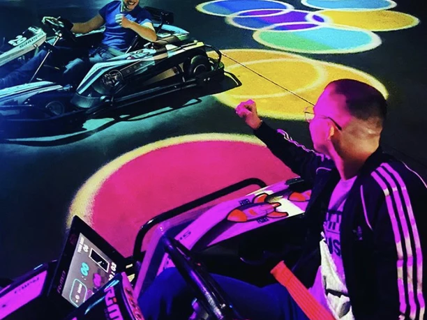 Snake Duo.jpg Zwei Personen fahren in Go-Karts, umgeben von bunten Lichtern auf dem Boden.