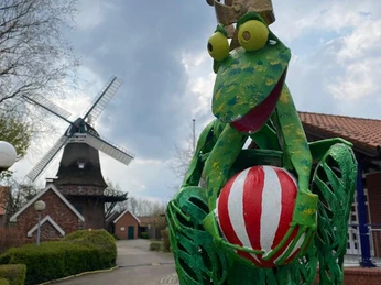 Frosch an der Badewanne Ein metallener Frosch mit Krone und buntem Ball steht vor einer historischen Windmühle.