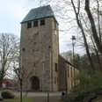Schöpfungslehrpfad Holsten-Bexten Steinkirche mit hohem Turm und kupfernem Dach, umgeben von Bäumen am Rand eines Waldwegs