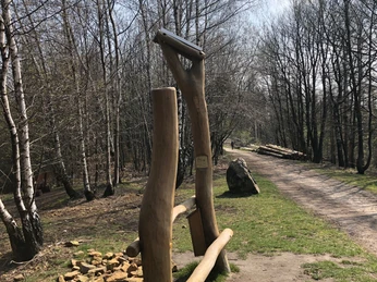 Hörstele Kammweg Oerlinghausen Holzskulptur am Waldrand entlang eines Schotterwegs, umgeben von kahlen Bäumen im Frühling.