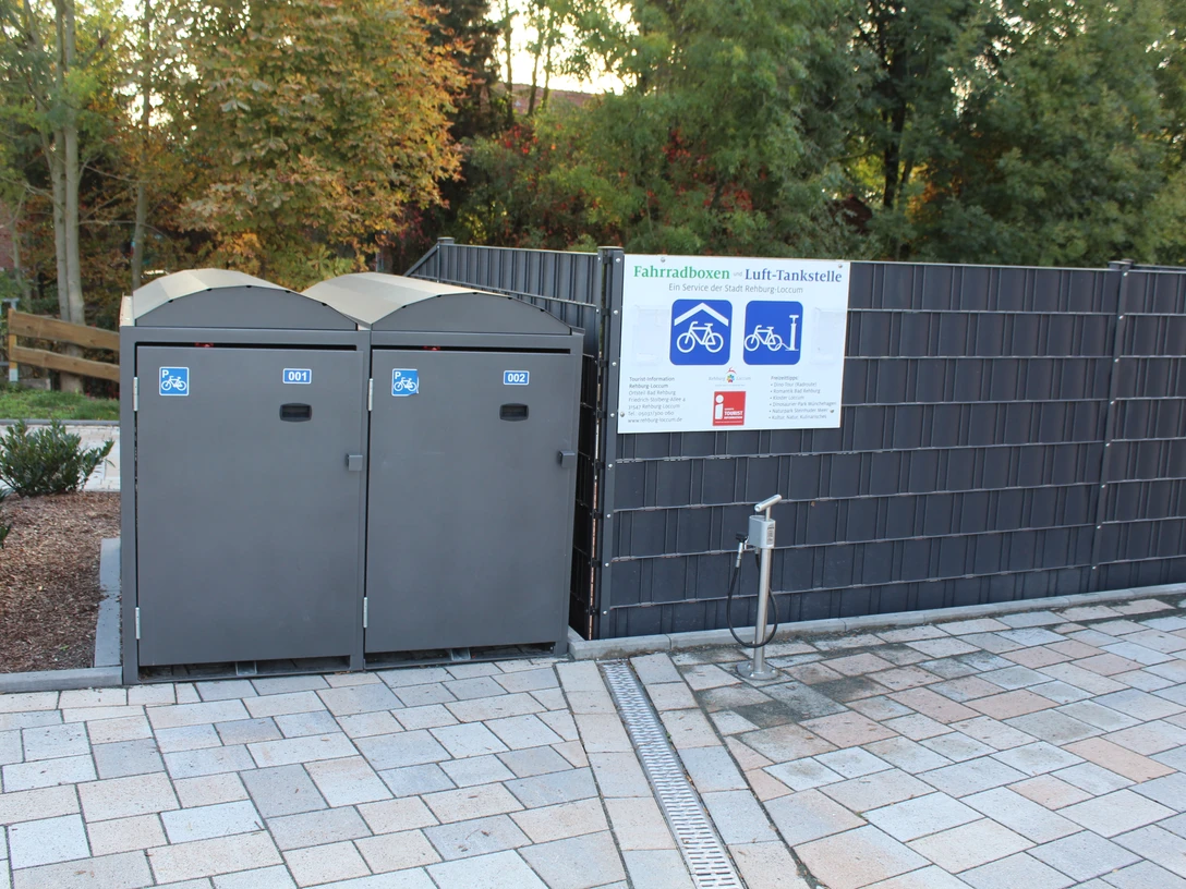 Fahrradboxen und Lufttankstelle Rehburg Barrierefreie Fahrradboxen und Lufttankstelle in Rehburg, umgeben von Bäumen und Plattenweg.