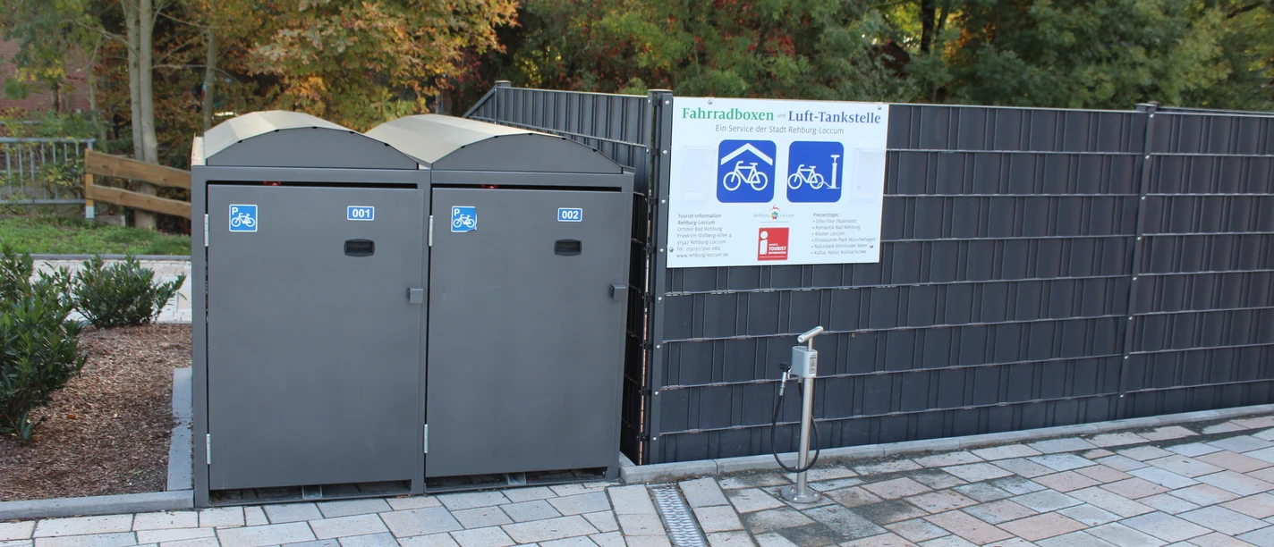 Fahrradboxen und Lufttankstelle Rehburg Barrierefreie Fahrradboxen und Lufttankstelle in Rehburg, umgeben von Bäumen und Plattenweg.
