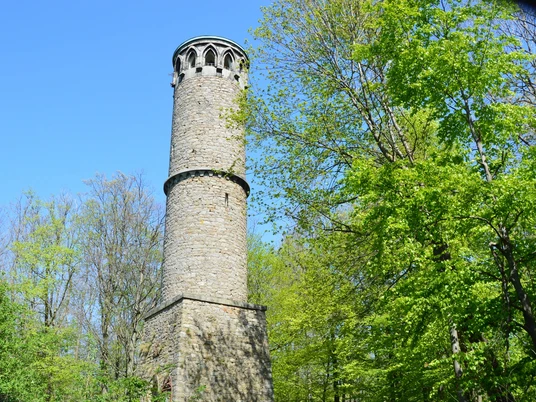 Kahlenbergturm Runder steinerner Aussichtsturm im Kahlenbergwald, von üppigem Frühlingslaub umgeben, bei klarem Himmel.