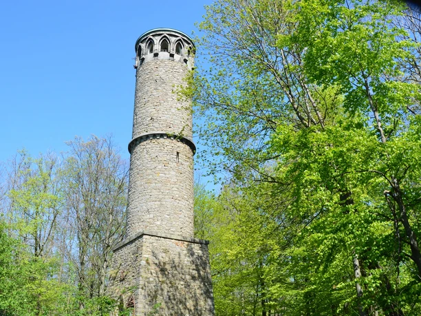 Kahlenbergturm Runder steinerner Aussichtsturm im Kahlenbergwald, von üppigem Frühlingslaub umgeben, bei klarem Himmel.
