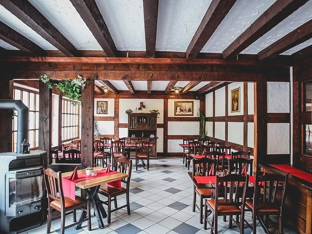 Restaurant Gemütlicher Gastraum im rustikalen Stil mit Holzbalken, Kamin und rot gedeckten Tischen.