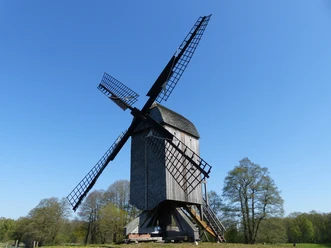 Historic trestle windmill in Dudensen, surrounded by meadows and trees under a blue sky.