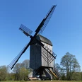 Historische Bockwindmühle in Dudensen, umgeben von Wiesen und Bäumen unter blauem Himmel.