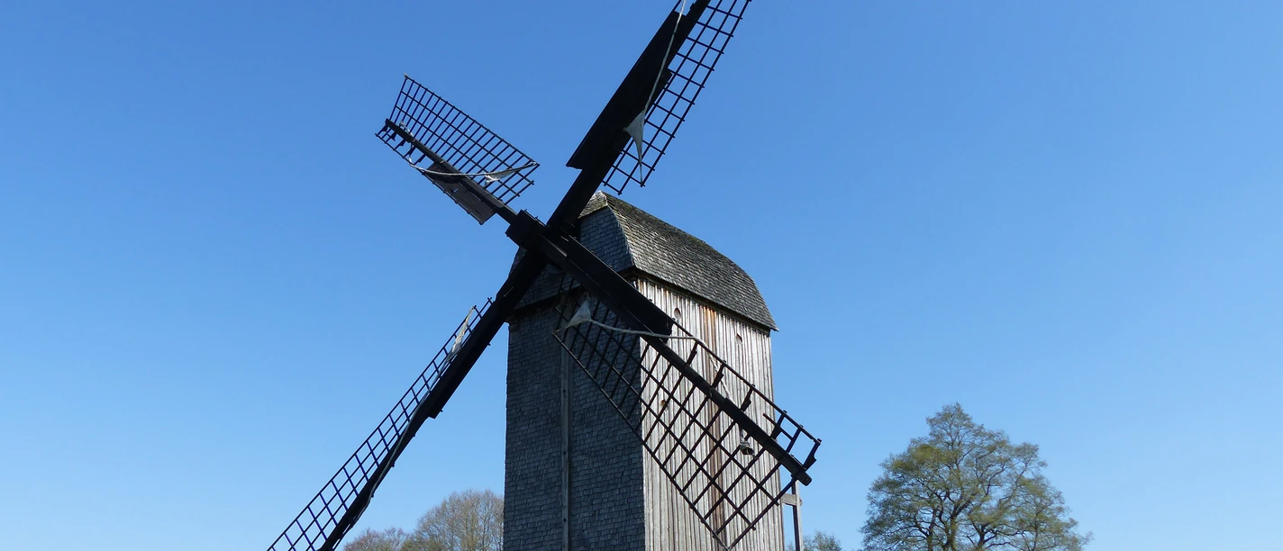 Historic trestle windmill in Dudensen, surrounded by meadows and trees under a blue sky.