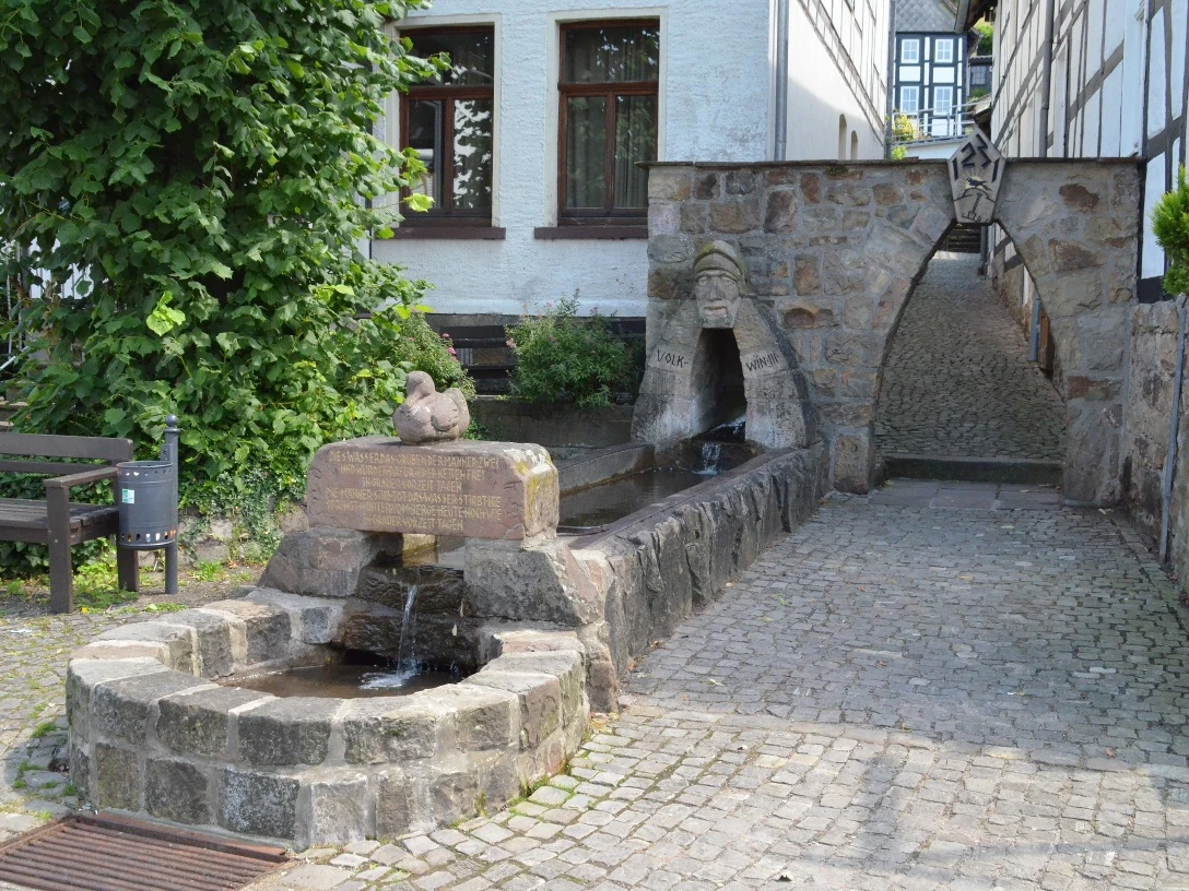 Volkwinbrunnen Ein steinerner Brunnen mit Wasserbecken und Relief, umgeben von gepflastertem Hof und Fachwerkhäusern.