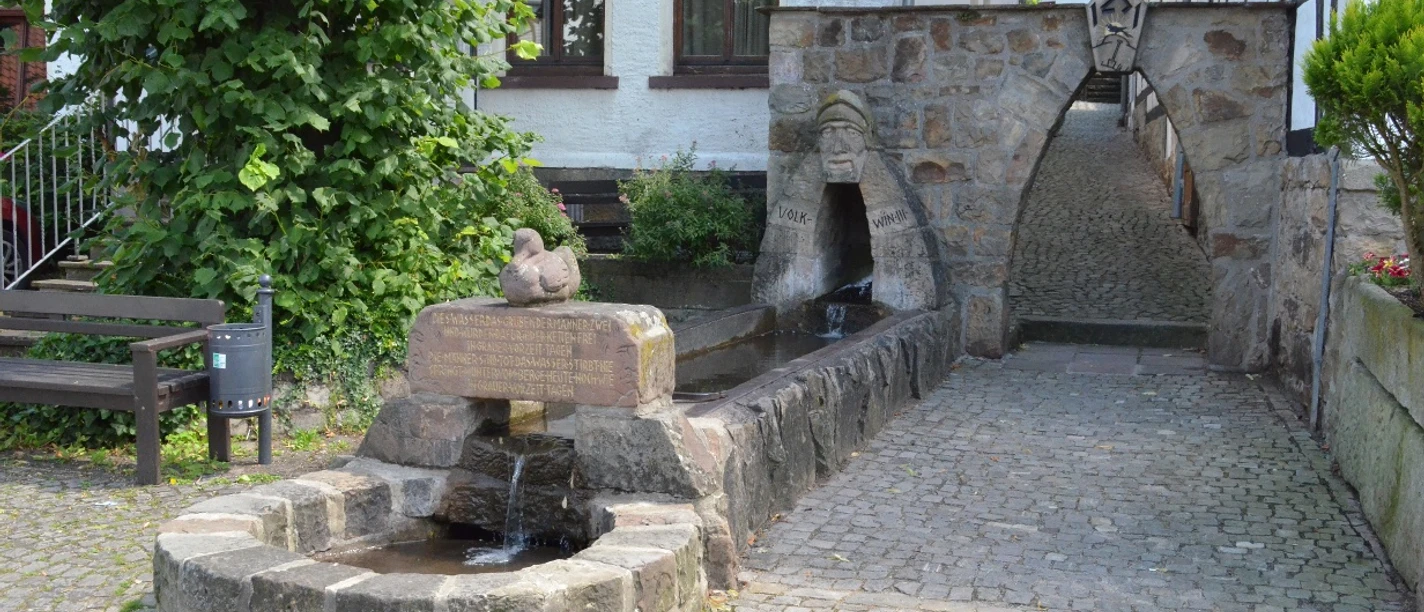Volkwinbrunnen Ein steinerner Brunnen mit Wasserbecken und Relief, umgeben von gepflastertem Hof und Fachwerkhäusern.