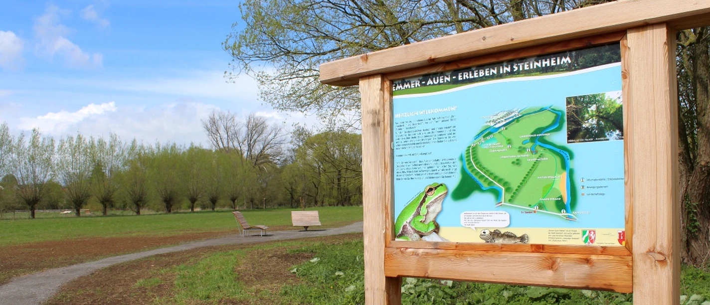 Infoschild Emmerauen Weg Infoschild zum Emmerauen Weg mit Karte, Beschreibung und Bildern in einer grünen Parklandschaft.