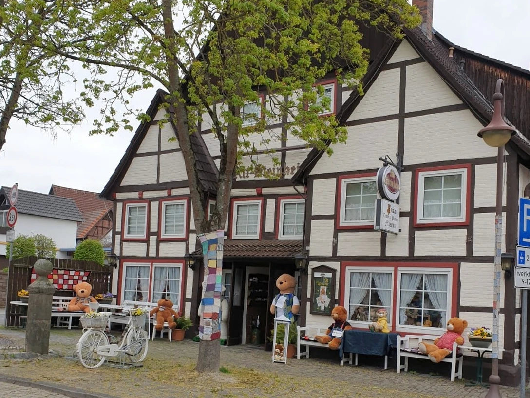 Teddy- und Puppenmuseum Fachwerkhaus mit bunten Puppen und Teddybären, umgeben von Bäumen und einer ruhigen Straße.