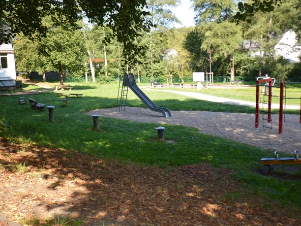 Mehrgenerationenpark Schönenberg.jpg Spielplatz mit Rutsche, Schaukeln und Wippen, umgeben von grünen Bäumen und Rasenflächen.