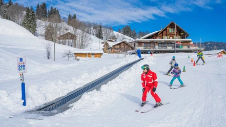 Skilehrer mit Kindern am Übungshang mit Förderband bei bestem Winterwetter