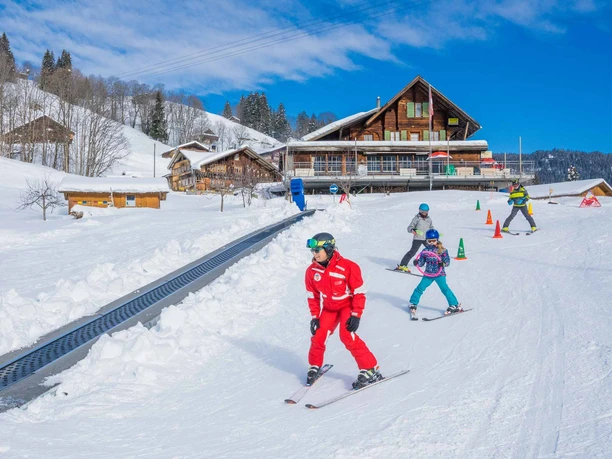 Skilehrer mit Kindern am Übungshang mit Förderband bei bestem Winterwetter
