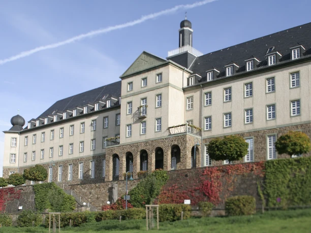 Kardinal-Schulte Haus Historisches Gebäude mit symmetrischer Fassade, prächtigen Büschen und blauem Himmel im Hintergrund.