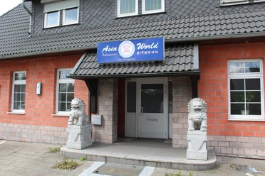 Eingangsbereich des Asia World Nienburg mit zwei steinernen Wächterlöwen und Backsteinfassade.