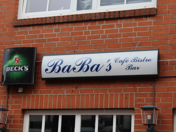 Baba's Bistro met een uitnodigende ingang in een bakstenen gebouw, geflankeerd door lantaarns en een bierbordje.
