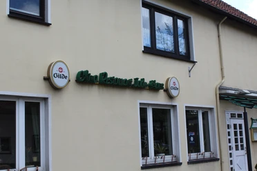 Das Jadehaus ist ein Lokal mit gelber Fassade, grüner Beschilderung und weißen Fensterrahmen.