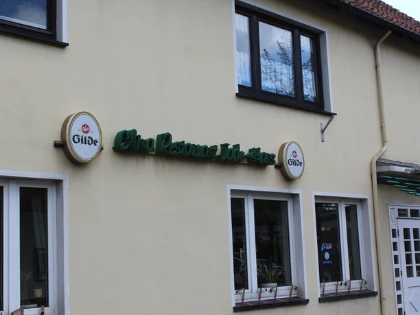 Jadehaus Das Jadehaus ist ein Lokal mit gelber Fassade, grüner Beschilderung und weißen Fensterrahmen.