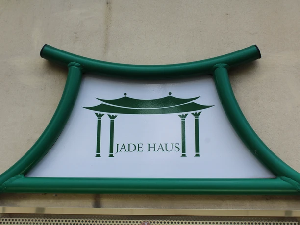 Jadehaus Das "Jadehaus" Schild mit grünem Rahmen zeigt ein stilisiertes Gebäude auf weißem Hintergrund.