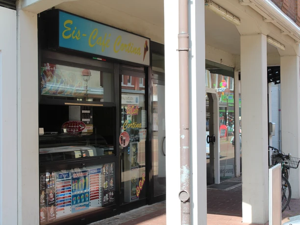 Eiscafé Cortina with large window, colorful ice cream advertising and bicycle stand at the entrance.