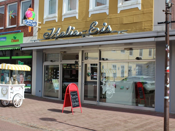 Ice cream café with yellow lettering and sales trolley in front of the glass façade, adjacent to a store.