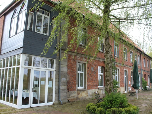 Hasbergscher Hof Roter Backsteinbau mit großen Fenstern, umgeben von frischem Grün und blühenden Bäumen.