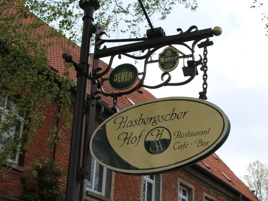 Hasbergscher Hof Hinweisschild des Hasbergscher Hofs mit stilvollem Wappen, umgeben von rotem Ziegelgebäude.