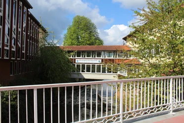 Brückenrestaurant Ein Restaurant auf einer Fußgängerbrücke verbindet zwei Gebäude über einem Fluss in üppiger Natur.
