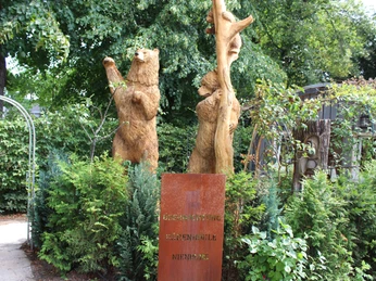 KreativWerkstatt am Wall Holzskulpturen von Bären, umgeben von grünem Laub und niedrigen Büschen, im Freien platziert.Wooden sculptures of bears, surrounded by green foliage and low bushes, placed outdoors.Træskulpturer af bjørne, omgivet af grønt løv og lave buske, placeret udendørs.Houten beelden van beren, omringd door groen en lage struiken, buiten geplaatst.