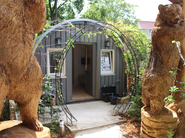 FeWo Bärenhöhle - KreativWerkstatt am Wall Ein kleines, hölzernes Ferienhäuschen mit Bärenstatuen am Eingang in einer grünen Umgebung.