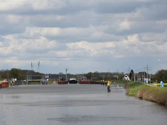 Die Schleuse Dörverden mit vorbeifahrendem Schiff, umgeben von grünen Wiesen und rostroten Strukturen.